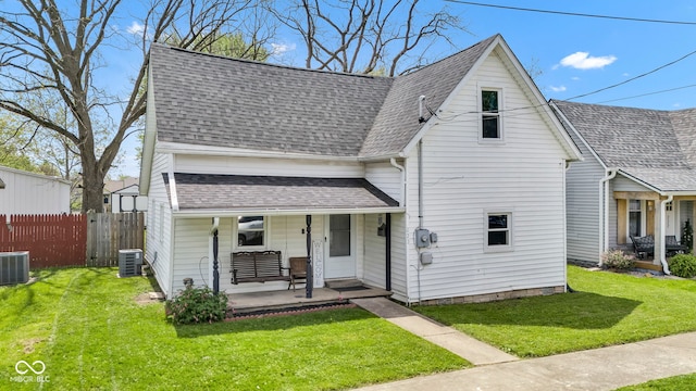 view of front of house featuring covered porch, roof with shingles, fence, cooling unit, and a front lawn