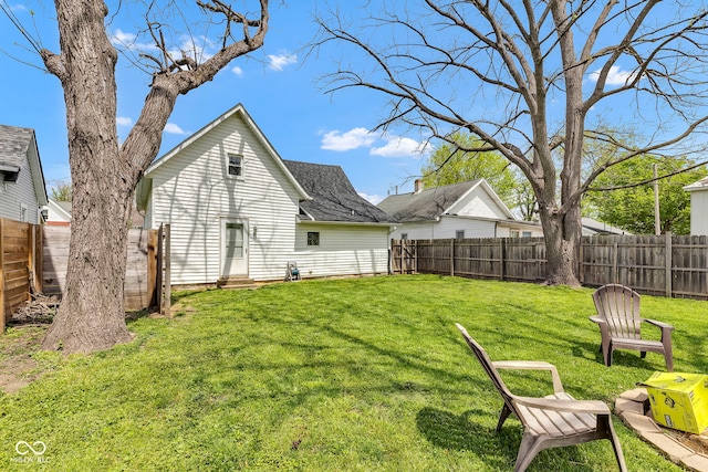 back of property with a yard, roof with shingles, a fenced backyard, and entry steps