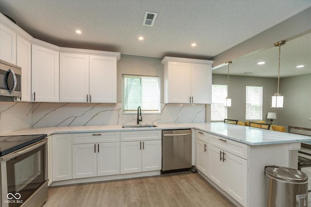 kitchen with a sink, stainless steel appliances, a peninsula, a wealth of natural light, and visible vents