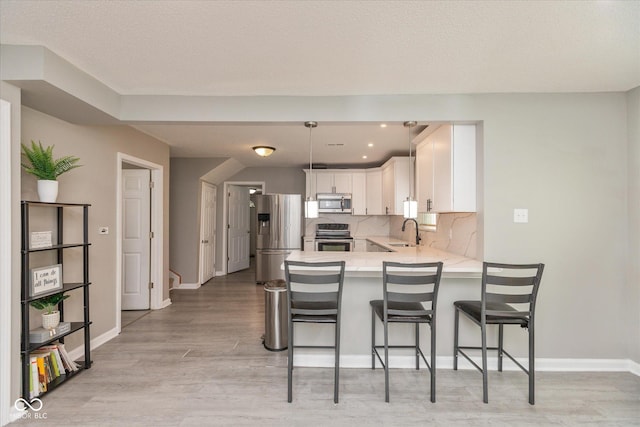 kitchen with appliances with stainless steel finishes, light countertops, a sink, white cabinets, and a peninsula