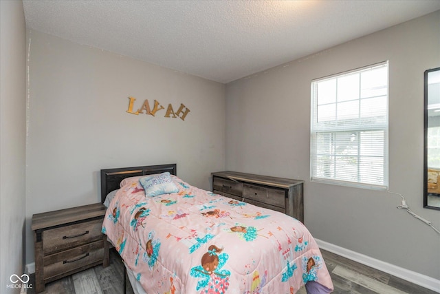 bedroom featuring baseboards, multiple windows, a textured ceiling, and wood finished floors