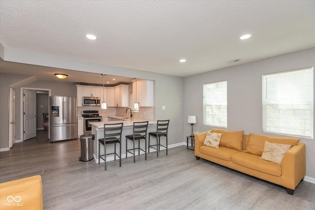 living room featuring recessed lighting, baseboards, a textured ceiling, and light wood-style floors