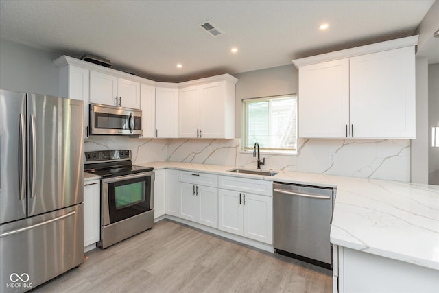 kitchen with visible vents, light stone counters, a sink, light wood finished floors, and stainless steel appliances
