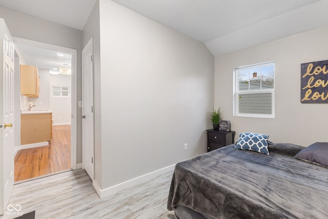 bedroom with baseboards, a sink, light wood-style flooring, and vaulted ceiling