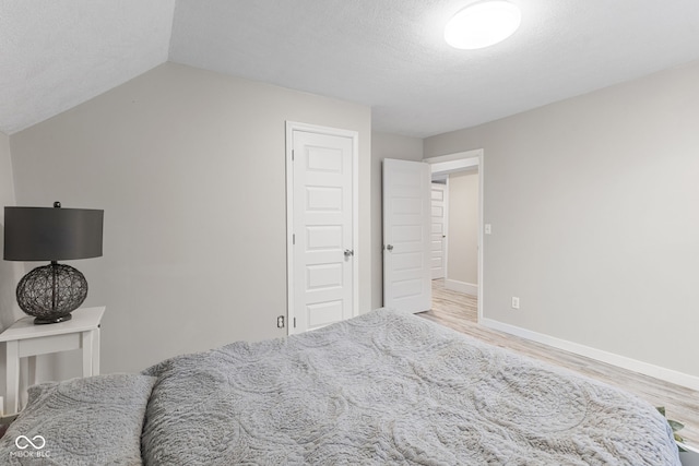 bedroom featuring a textured ceiling, baseboards, vaulted ceiling, and wood finished floors