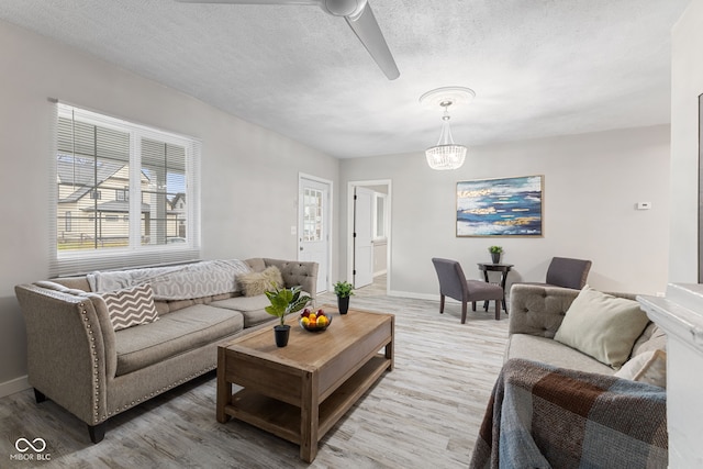 living room featuring a textured ceiling, baseboards, ceiling fan with notable chandelier, and light wood-style floors