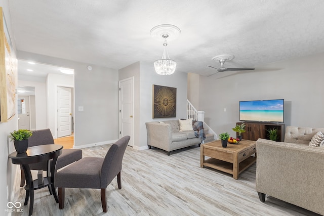 living area with baseboards, ceiling fan with notable chandelier, stairs, and light wood-style flooring