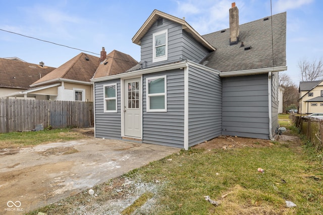 rear view of house featuring roof with shingles, fence, a chimney, and a patio area