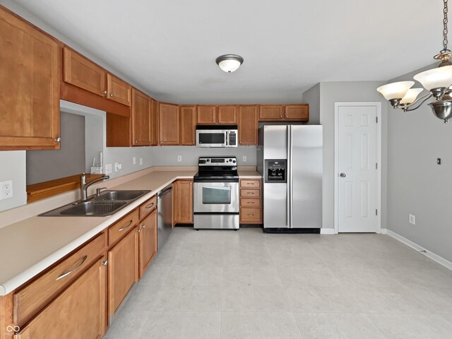 kitchen with brown cabinets, appliances with stainless steel finishes, a sink, light countertops, and a chandelier