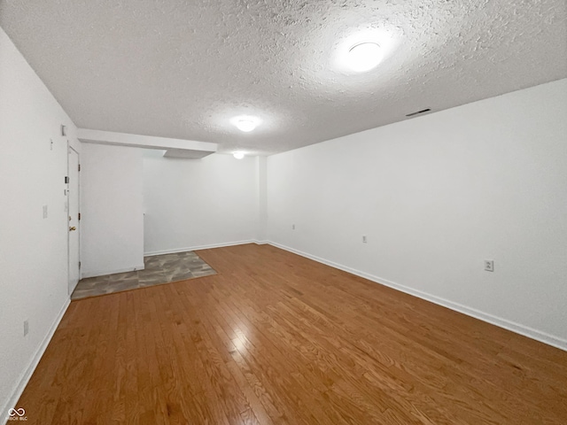 finished below grade area with baseboards, a textured ceiling, and wood finished floors