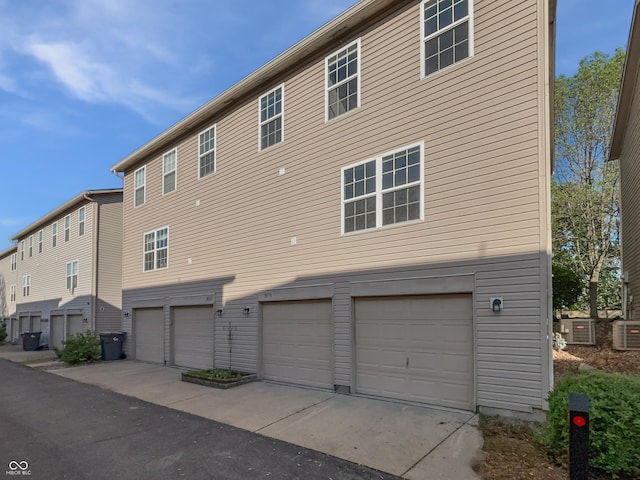 rear view of property with a garage, central AC, and driveway