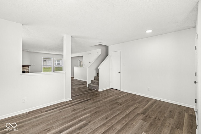 unfurnished living room with a textured ceiling, baseboards, stairs, and wood finished floors