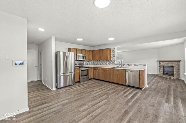 kitchen with brown cabinetry, wood finished floors, open floor plan, a sink, and appliances with stainless steel finishes