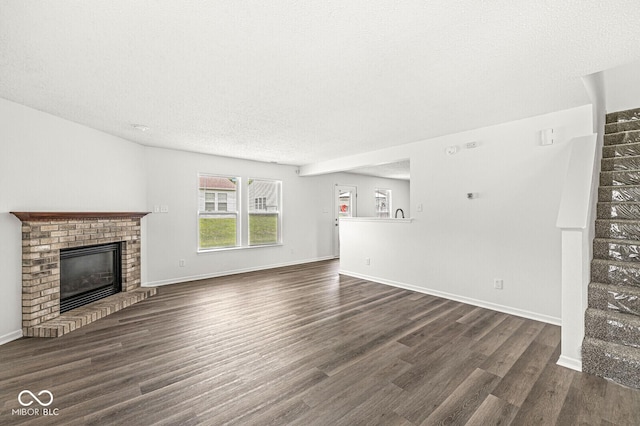 unfurnished living room featuring a fireplace, a textured ceiling, baseboards, dark wood-type flooring, and stairway