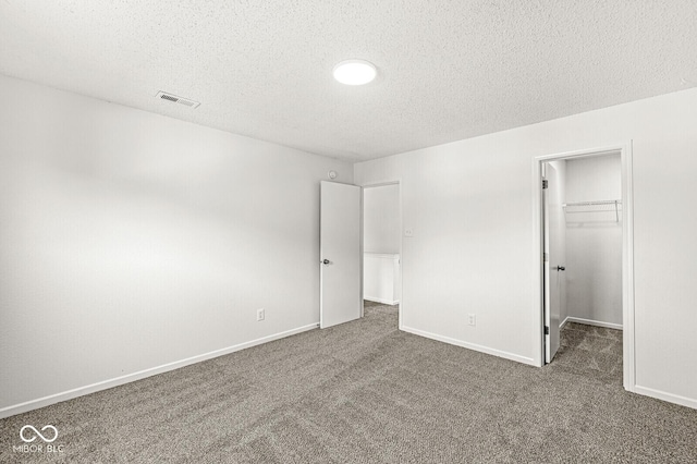 unfurnished bedroom featuring a textured ceiling, visible vents, a spacious closet, and carpet