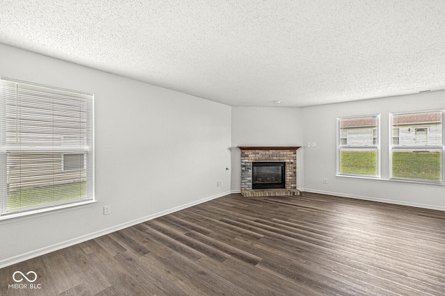 unfurnished living room with baseboards, a brick fireplace, dark wood finished floors, and a textured ceiling