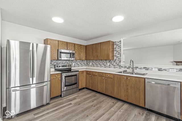 kitchen featuring a sink, light countertops, a textured ceiling, brown cabinetry, and stainless steel appliances