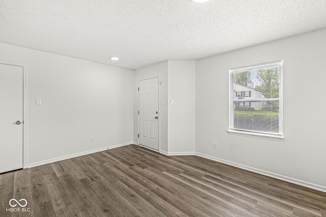 spare room featuring a textured ceiling, baseboards, and dark wood-type flooring