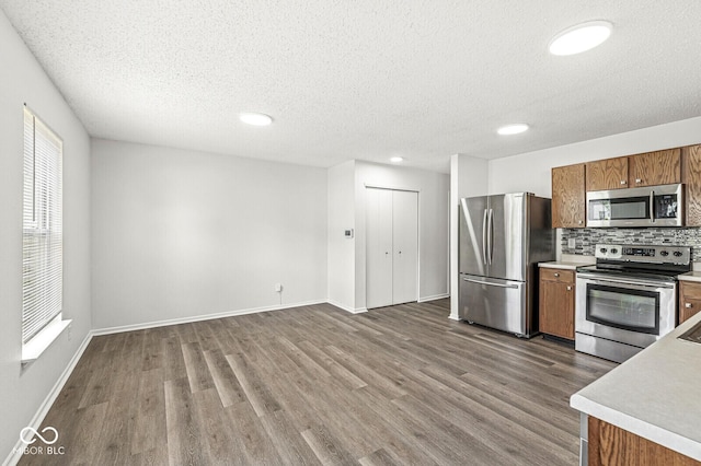 kitchen featuring light countertops, stainless steel appliances, brown cabinetry, and dark wood-style flooring