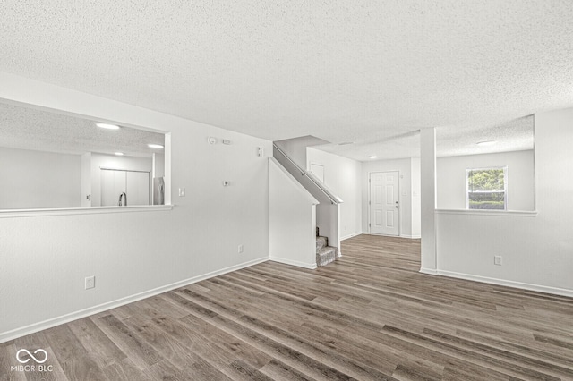 unfurnished living room featuring stairs, a textured ceiling, baseboards, and wood finished floors