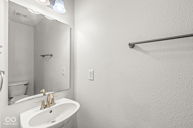 bathroom featuring toilet, visible vents, and a sink