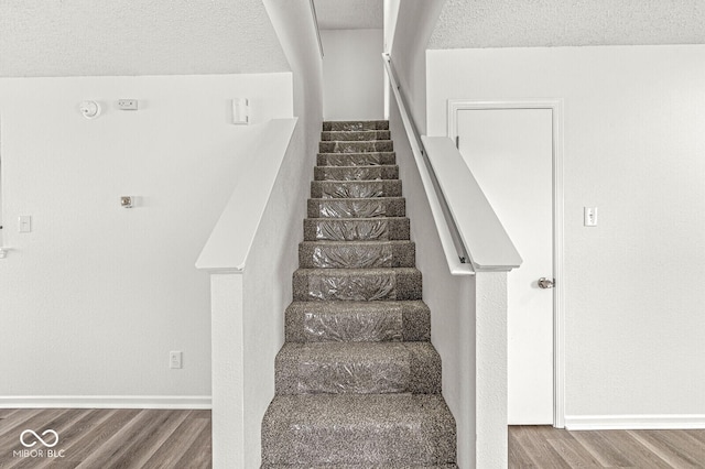 stairway with a textured ceiling, baseboards, and wood finished floors
