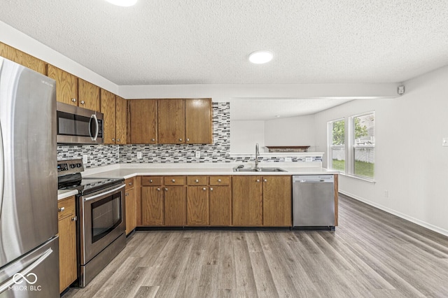 kitchen with brown cabinets, appliances with stainless steel finishes, a sink, and light wood-type flooring