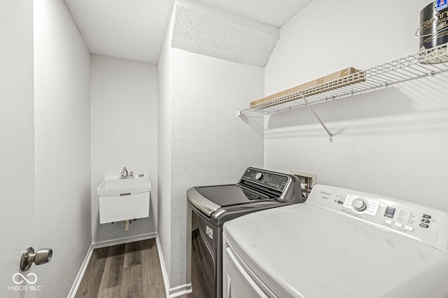 laundry area featuring laundry area, wood finished floors, baseboards, washer and clothes dryer, and a sink