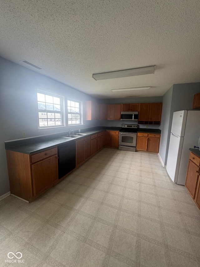 317 Legacy Blvd, Greenwood, IN 46143 - kitchen with brown cabinetry, a textured ceiling, dark countertops, appliances with stainless steel finishes, and a sink