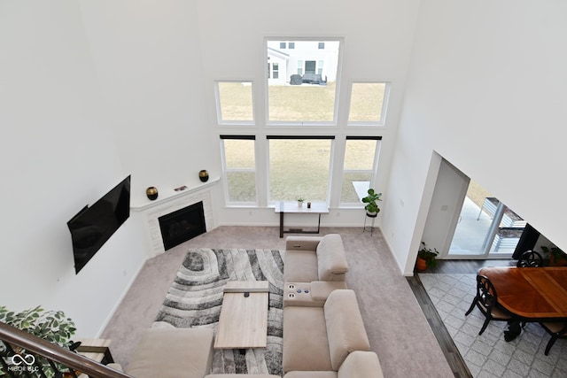 living room featuring carpet flooring, a high ceiling, baseboards, and a fireplace