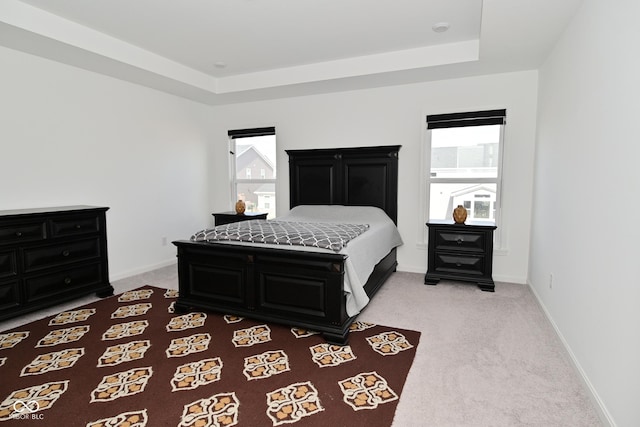 bedroom with baseboards, light carpet, and a tray ceiling