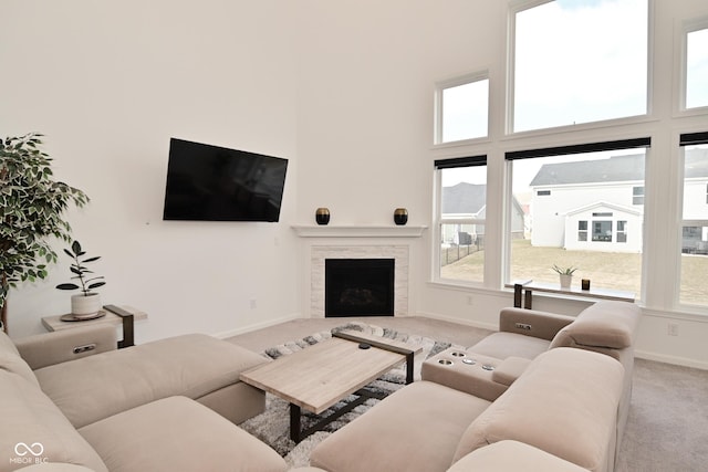 living area featuring carpet floors, baseboards, a stone fireplace, and a high ceiling