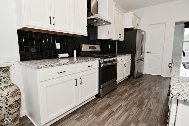 kitchen featuring dark wood-style flooring, wall chimney range hood, white cabinetry, appliances with stainless steel finishes, and backsplash