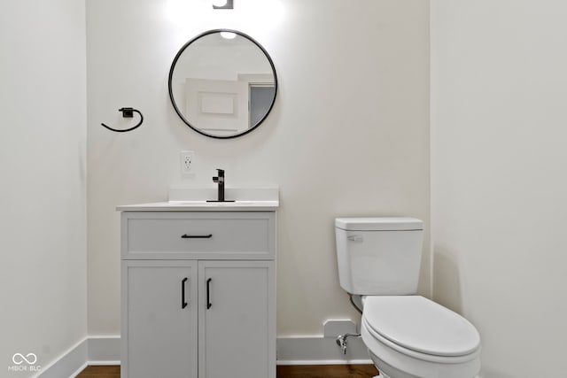 half bath with vanity, baseboards, and toilet