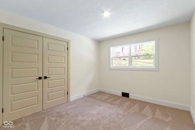 carpeted spare room with baseboards, a textured ceiling, and visible vents