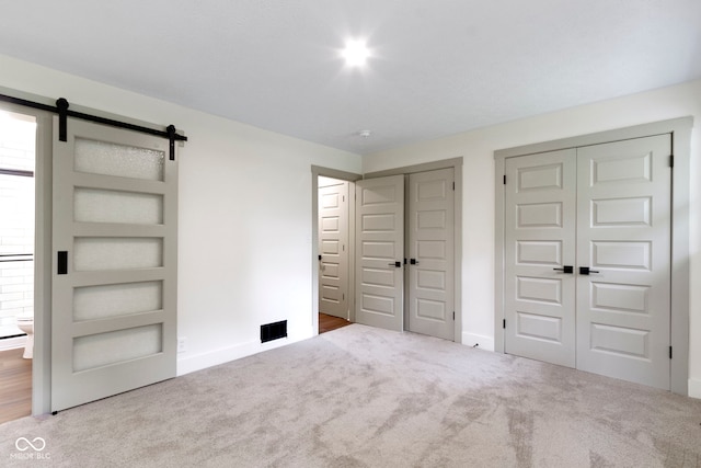 unfurnished bedroom featuring carpet floors, baseboards, two closets, and a barn door