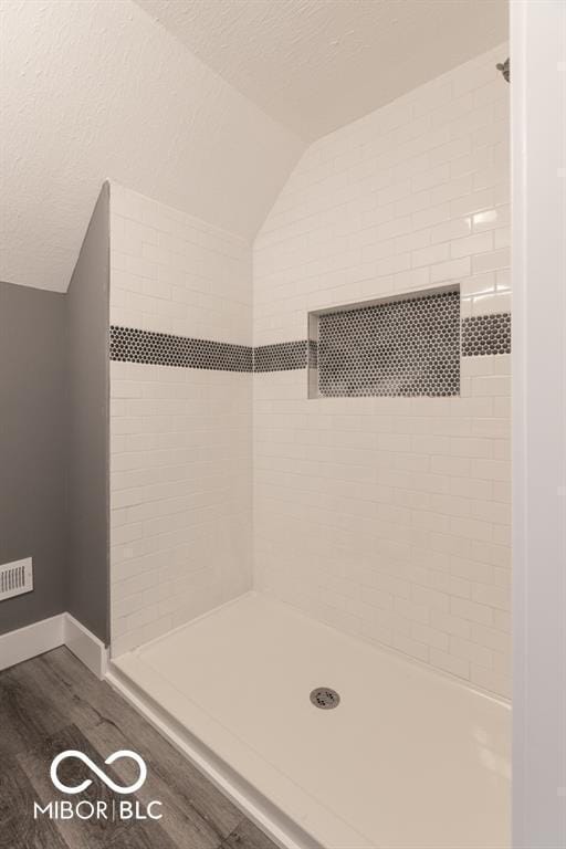 bathroom with wood finished floors, a tile shower, lofted ceiling, baseboards, and a textured ceiling