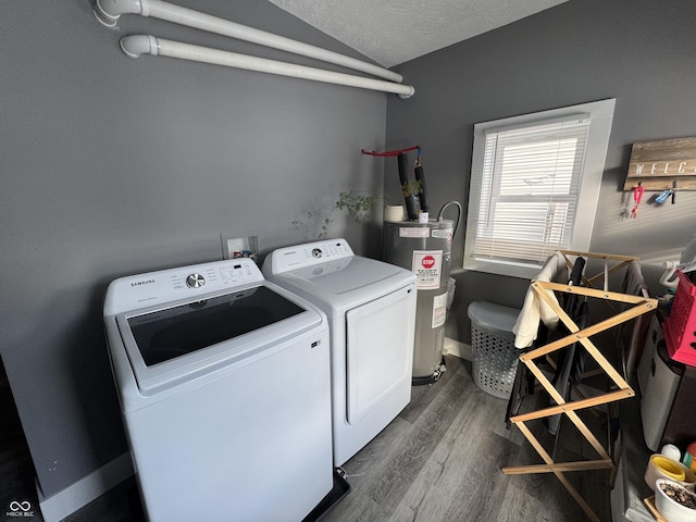 washroom featuring electric water heater, washing machine and clothes dryer, dark wood finished floors, baseboards, and a textured ceiling
