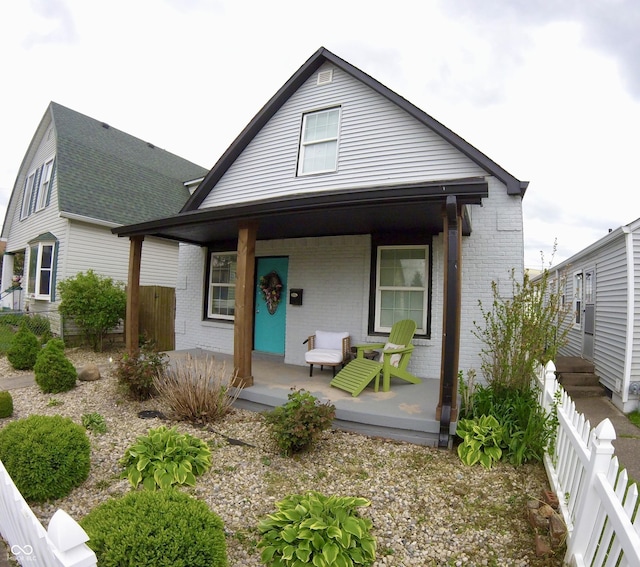 bungalow featuring covered porch, brick siding, fence, and a shingled roof