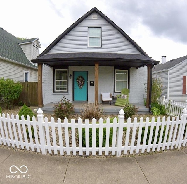 bungalow-style house featuring a porch, brick siding, and a fenced front yard