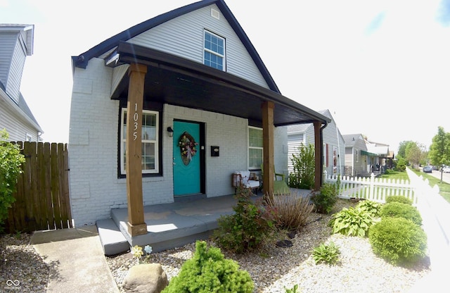 bungalow-style house with a porch, brick siding, and fence