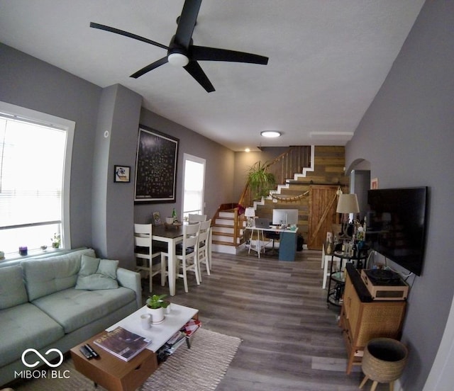 living area with stairs, a ceiling fan, and wood finished floors
