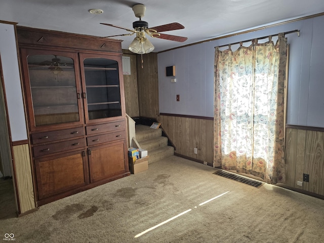 carpeted spare room featuring a ceiling fan, wooden walls, stairs, plenty of natural light, and wainscoting