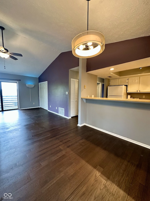 unfurnished living room featuring a textured ceiling, dark wood finished floors, a ceiling fan, baseboards, and vaulted ceiling