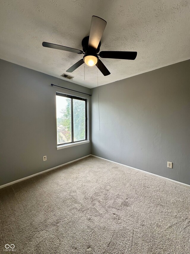 carpeted empty room with baseboards, a textured ceiling, visible vents, and ceiling fan