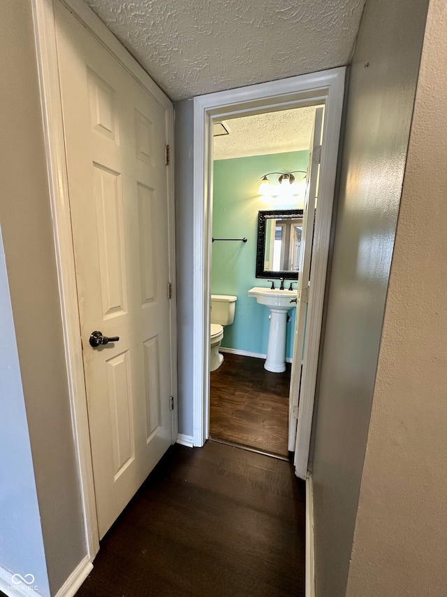 corridor with a sink, baseboards, a textured ceiling, and dark wood-type flooring