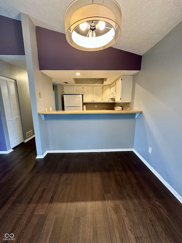 kitchen featuring freestanding refrigerator, a peninsula, wood finished floors, baseboards, and white cabinetry