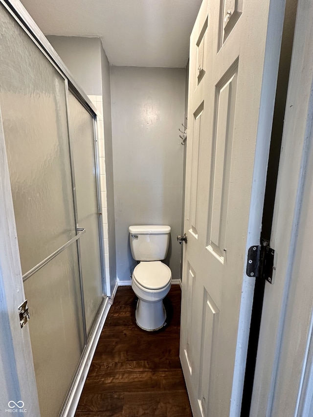 bathroom with toilet, baseboards, a shower stall, and wood finished floors