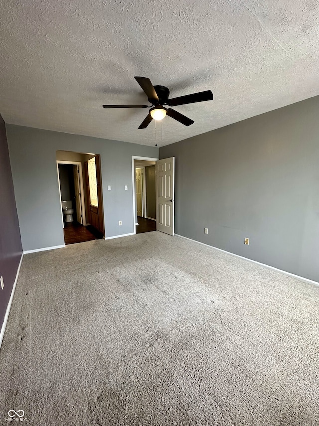 unfurnished bedroom featuring ceiling fan, ensuite bath, a textured ceiling, dark carpet, and baseboards
