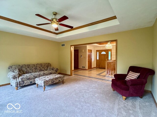 living area featuring a raised ceiling, baseboards, carpet floors, and ceiling fan